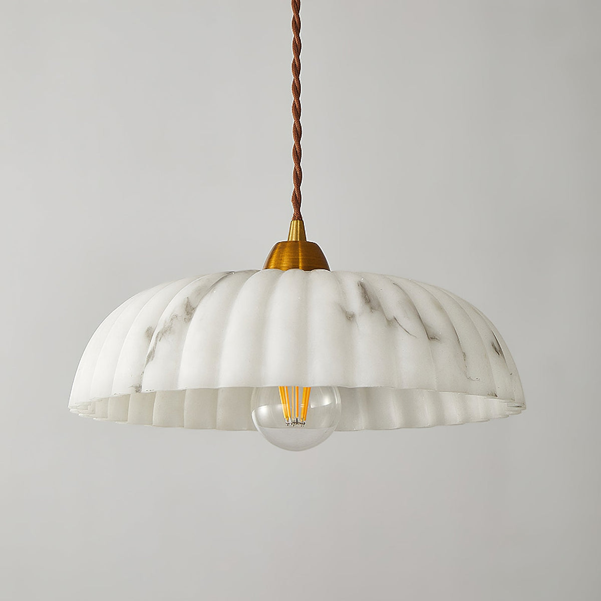 A Clérachic pendant with a shallow ribbed white shade, a gold cap and a visible filament bulb, on a light grey backdrop.
