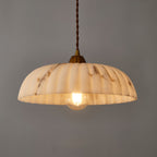 A Clérachic pendant glowing warm, with a cream shade veined in brown, against a dark grey wall.