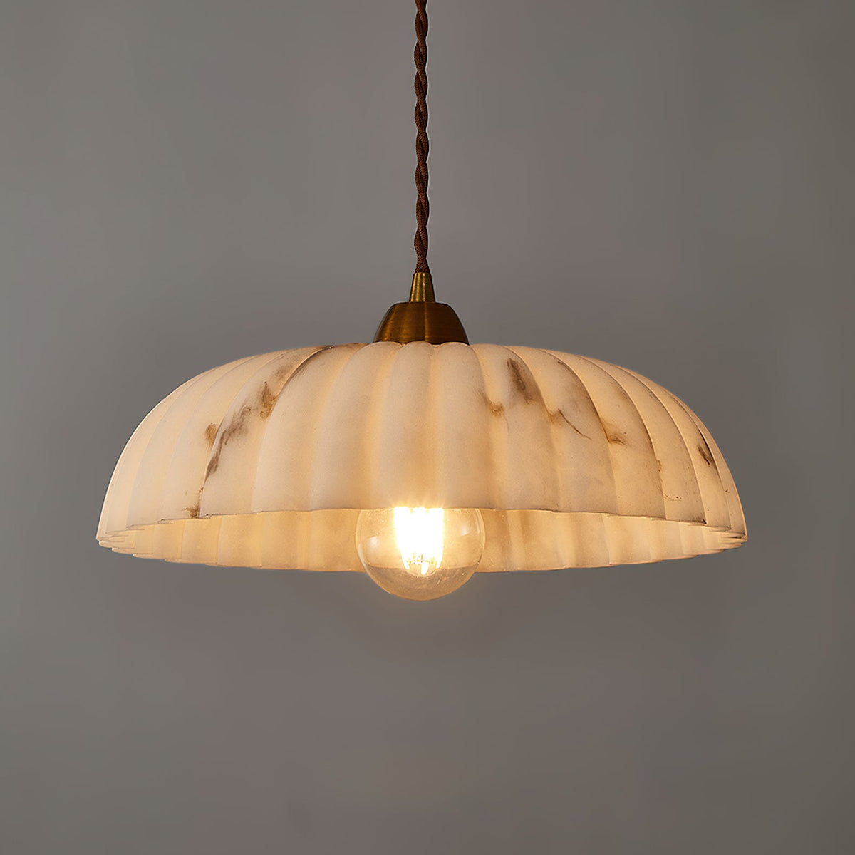 A Clérachic pendant glowing warm, with a cream shade veined in brown, against a dark grey wall.