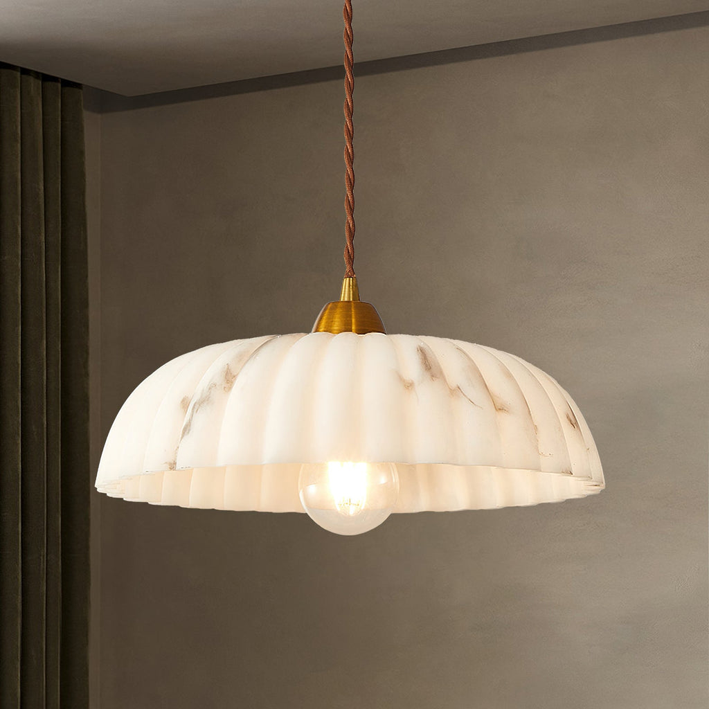 Lit Clérachic pendant with a ribbed marbled shade and a gold cap, hanging in front of a taupe wall and a dark curtain.