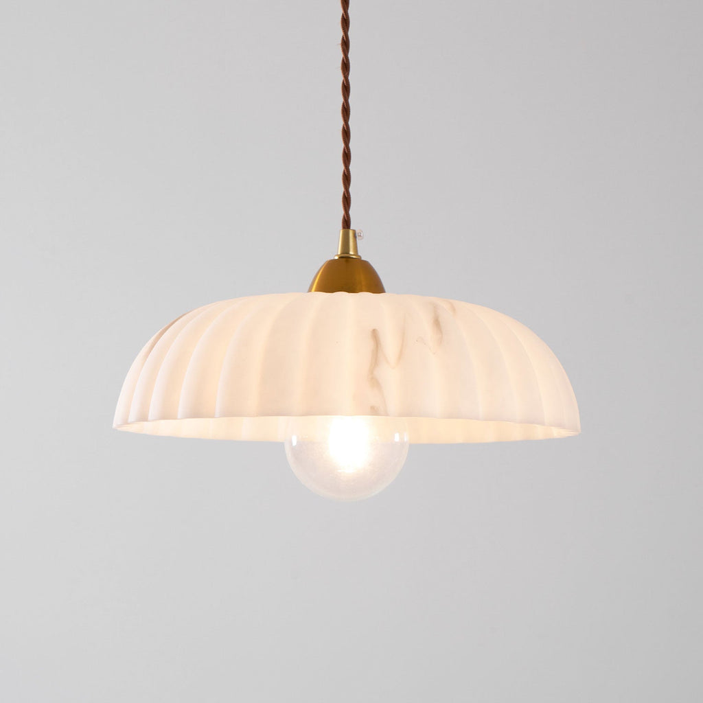 A Clérachic pendant with a peachy-white ribbed shade and a clear glass bulb, glowing on a pale grey backdrop.