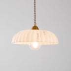 A Clérachic pendant with a peachy-white ribbed shade and a clear glass bulb, glowing on a pale grey backdrop.