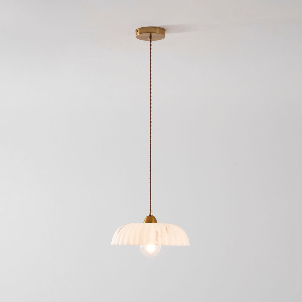 Full drop of a Clérachic pendant from a gold ceiling plate on a twisted brown cord to a small ribbed white shade.