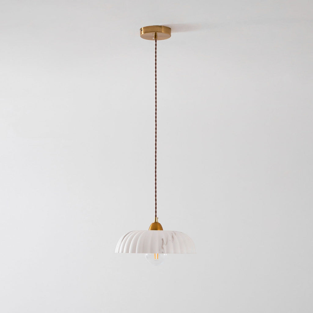 A small unlit Clérachic pendant hangs from a gold ceiling plate on a long twisted cord, with a pale ribbed shade at the bottom.