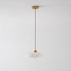 A small unlit Clérachic pendant hangs from a gold ceiling plate on a long twisted cord, with a pale ribbed shade at the bottom.