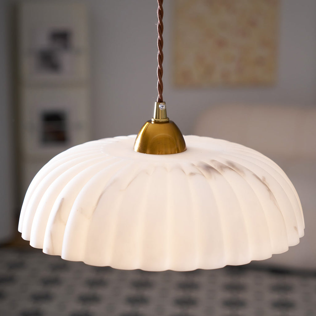 Close view of the large ribbed white shade and gold cap of this Clérachic pendant, with a soft-focus room behind.