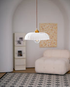 Small ribbed white Clérachic pendant in a pale arched room, with a cream armchair and a patterned tile rug below.
