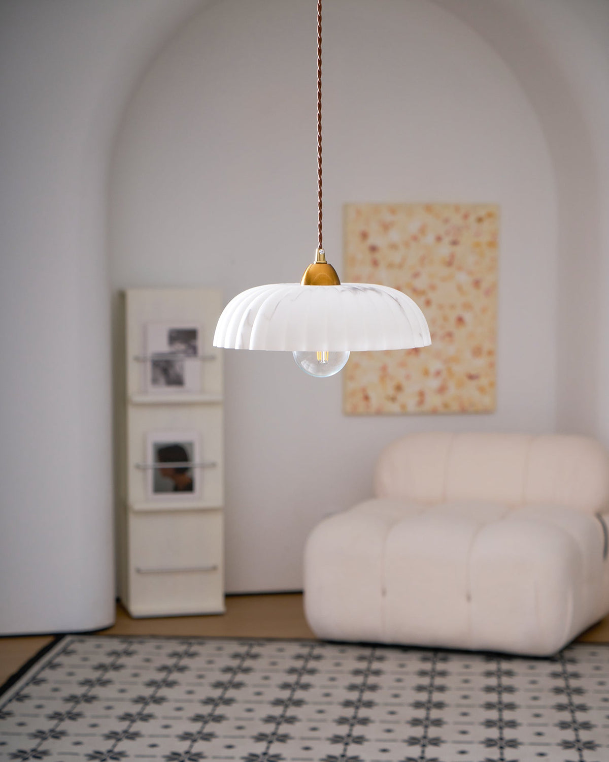 Small ribbed white Clérachic pendant in a pale arched room, with a cream armchair and a patterned tile rug below.