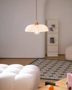 A small ribbed white Clérachic pendant in a pale room, with a bouclé ottoman and a pink vase in the foreground.
