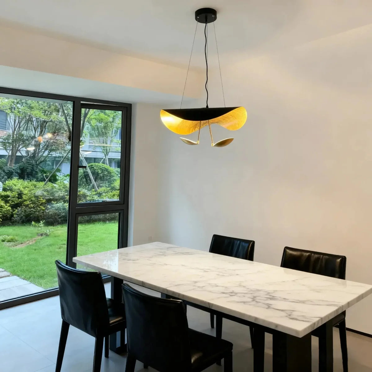 The black-and-gold Clérachic pendant light hangs low over a marble dining table lined with black leather chairs.