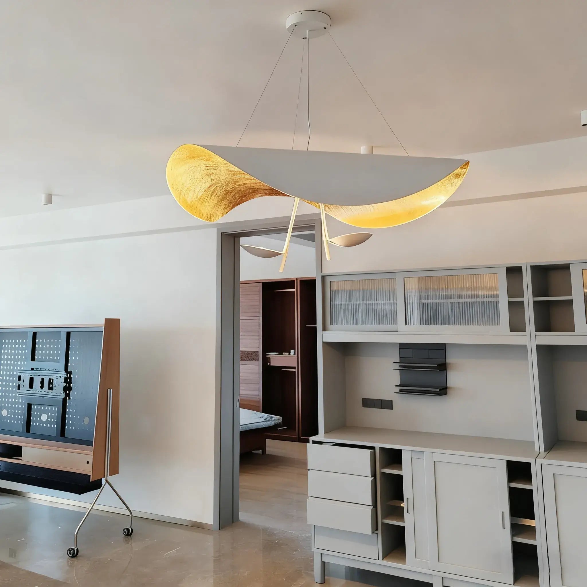 The gold-and-grey Clérachic pendant light glowing above a doorway between open shelving in a grey-toned living room.