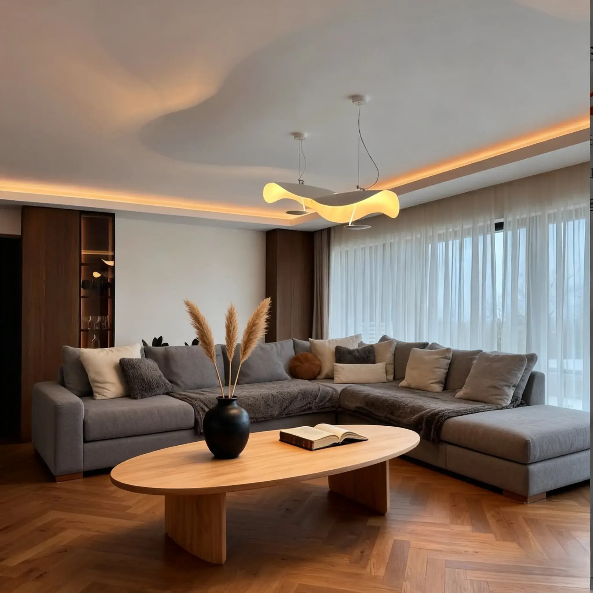 The Clérachic pendant light glowing above a grey sectional sofa, oval coffee table, and a vase of dried pampas grass.
