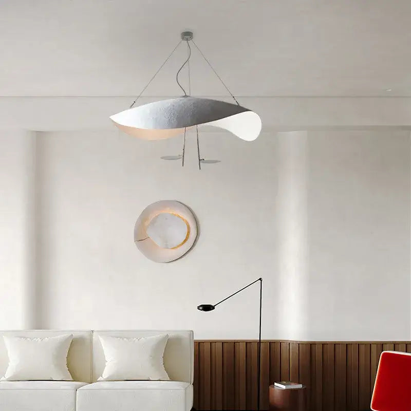 A pale Clérachic pendant light centred in a warm living room, near a round wall light and a black arc floor lamp.
