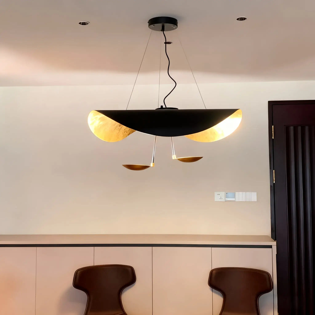 The black-and-gold Clérachic pendant light glowing above an entryway console beside a dark wood door and switch plate.
