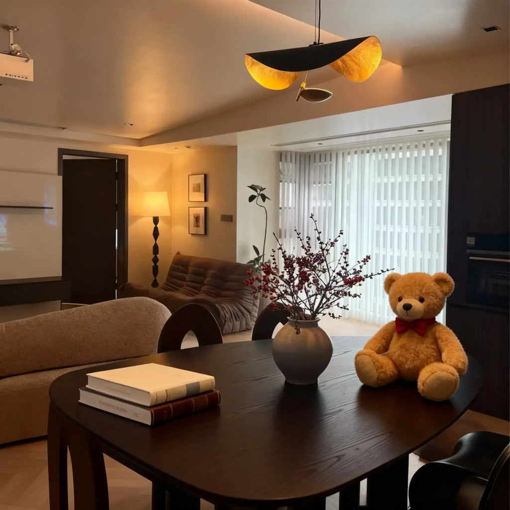 The black-and-gold Clérachic pendant light glows over a round table set with books, berry branches, and a toy bear.