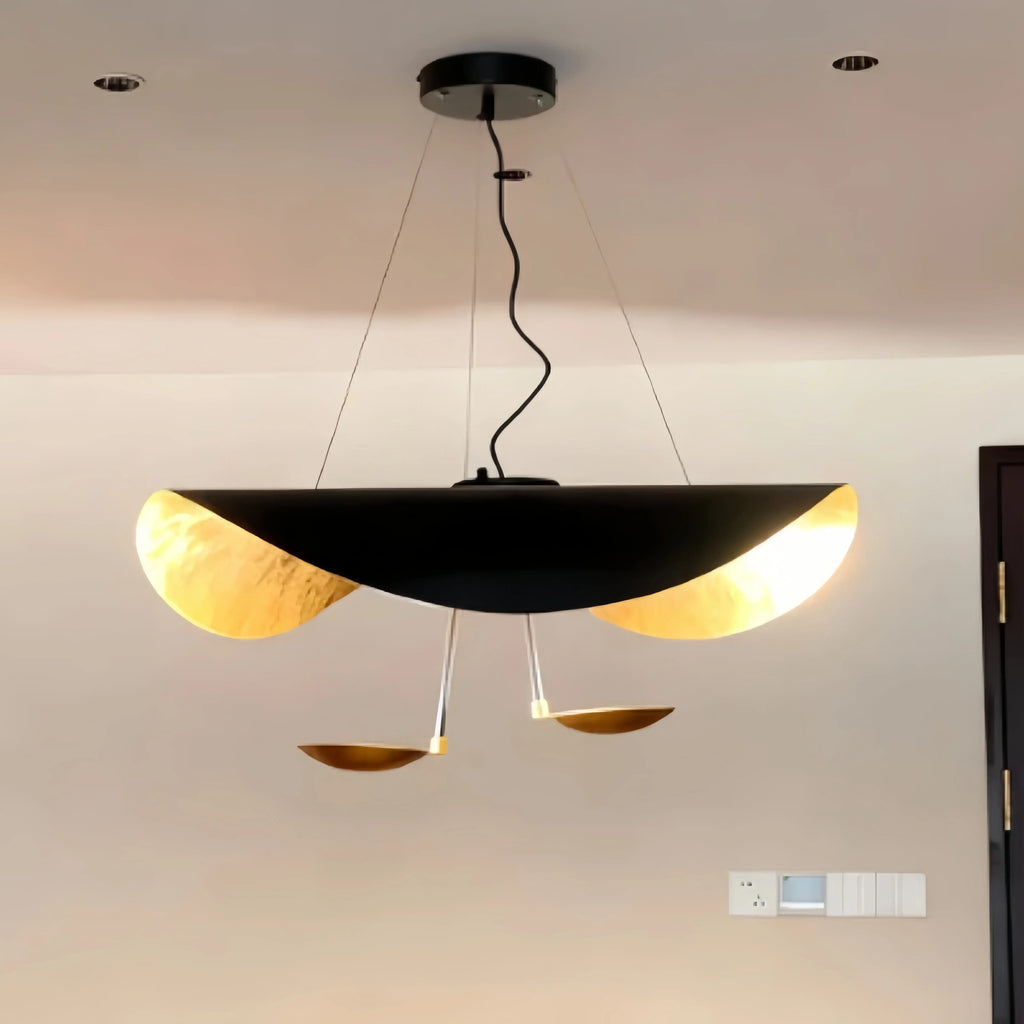 The white-and-gold Clérachic pendant light glows above a dining table beside a grey sectional and sheer curtains.