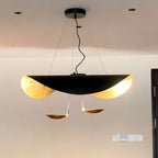 The white-and-gold Clérachic pendant light glows above a dining table beside a grey sectional and sheer curtains.