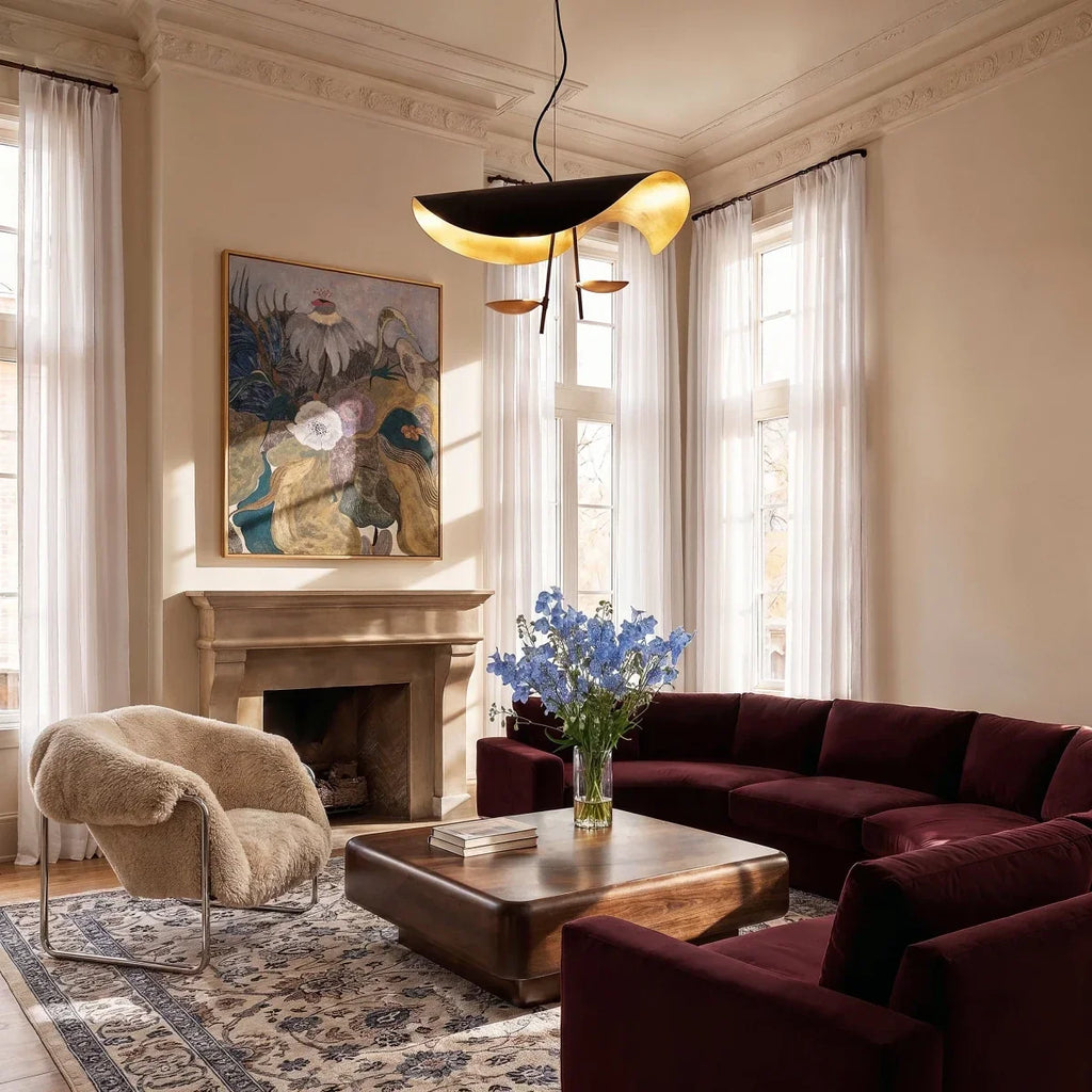 Clérachic two-light black pendant with gold-leaf shade hanging in a tall living room with a burgundy velvet sofa and a walnut table