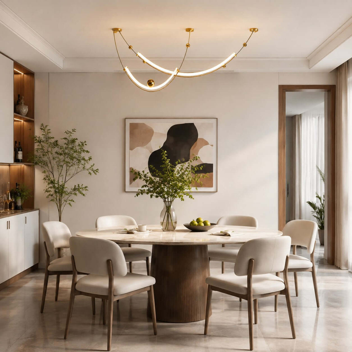 Curved gold-toned Clérachic pendant above a round pedestal dining table, with cream chairs and a built-in shelf unit at the side.