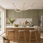 Clérachic pendant above a kitchen island with three cushioned oak stools, sage-green cabinets and a window on the left.