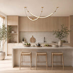 Glowing Clérachic pendant over a pale stone island with three woven-seat stools, in a kitchen of light wood cabinets.