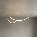 Close view of this Clérachic pendant on a grey plaster ceiling, its two lit curves joined by gold-toned wire and brass balls.
