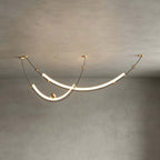 Close view of this Clérachic pendant on a grey plaster ceiling, its two lit curves joined by gold-toned wire and brass balls.