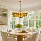 Green and gold disc chandelier from Clérachic hanging above a round pedestal dining table in a bright breakfast nook with tall windows.