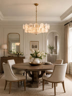 White glass disc chandelier from Clérachic above a round pedestal table, with cream upholstered chairs and a gilt mirror behind.