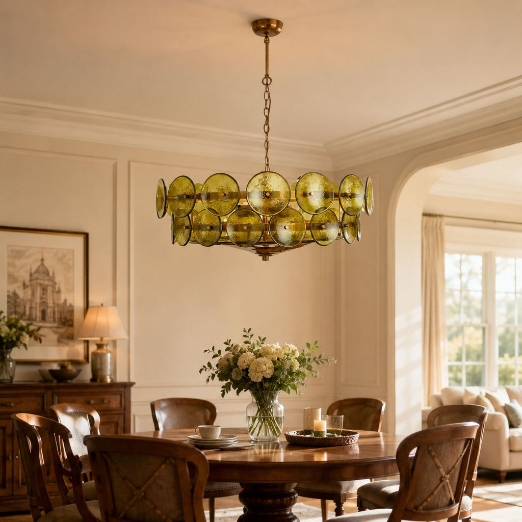 Olive-gold glass disc chandelier above a round wooden dining table with a vase of white flowers, shown as a Clérachic dining-room light.