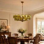 Olive-gold glass disc chandelier above a round wooden dining table with a vase of white flowers, shown as a Clérachic dining-room light.