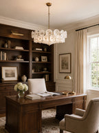 A white glass disc chandelier from Clérachic over a dark wood desk, with built-in bookshelves and a cream armchair beside it.