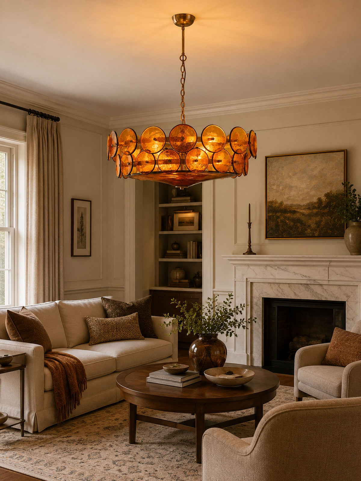 Lit amber glass discs on a Clérachic chandelier, over a round coffee table in a living room with a marble fireplace.