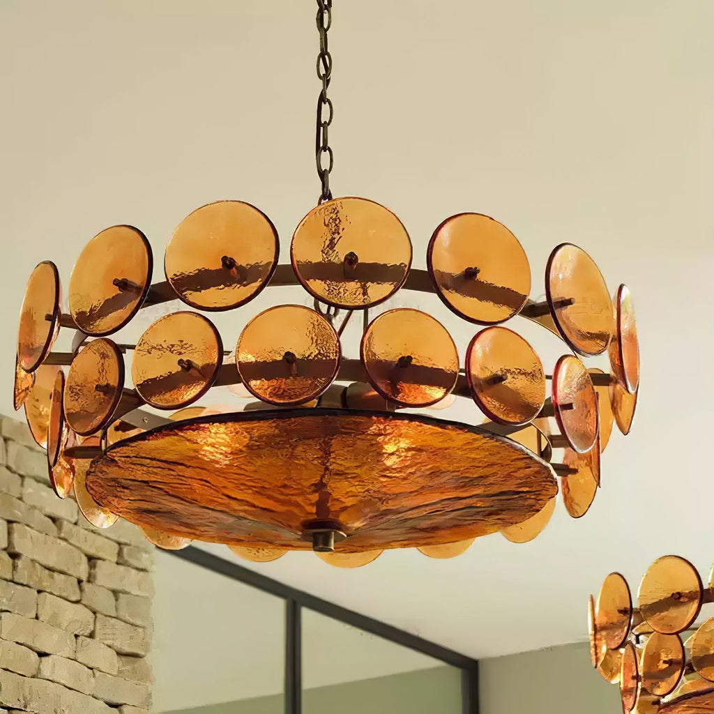 Looking up at the amber glass discs and the large textured bowl underneath this Clérachic chandelier, with a brick wall behind.