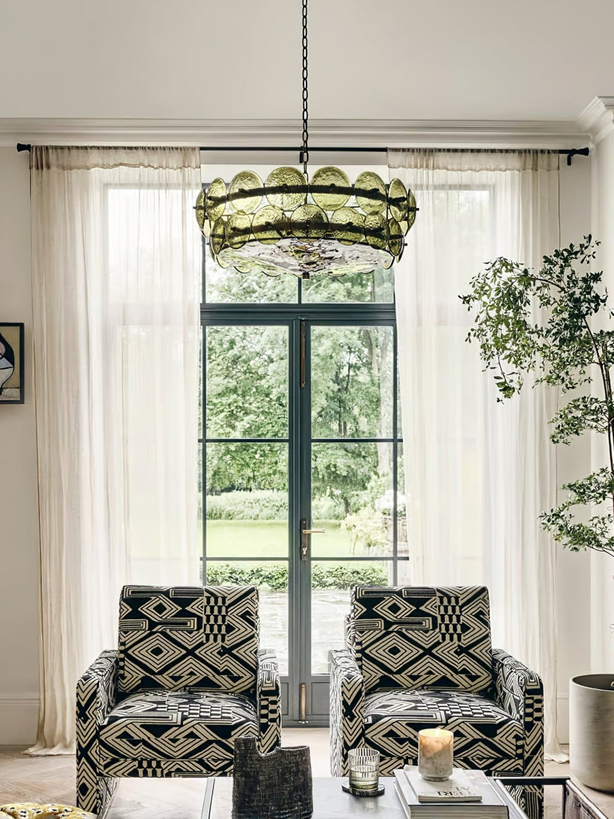 Green glass discs ring this Clérachic chandelier above two patterned armchairs, in front of French doors and sheer curtains.