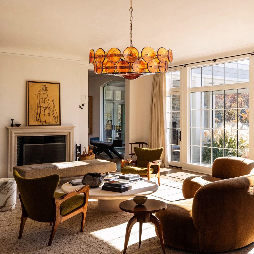 Amber disc chandelier from Clérachic over a pale round coffee table, with brown velvet seating and tall windows to the garden.