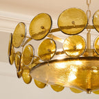 Detail of the hammered green-gold glass discs and the wide glass bowl underneath, on a Clérachic chandelier with a gold frame.