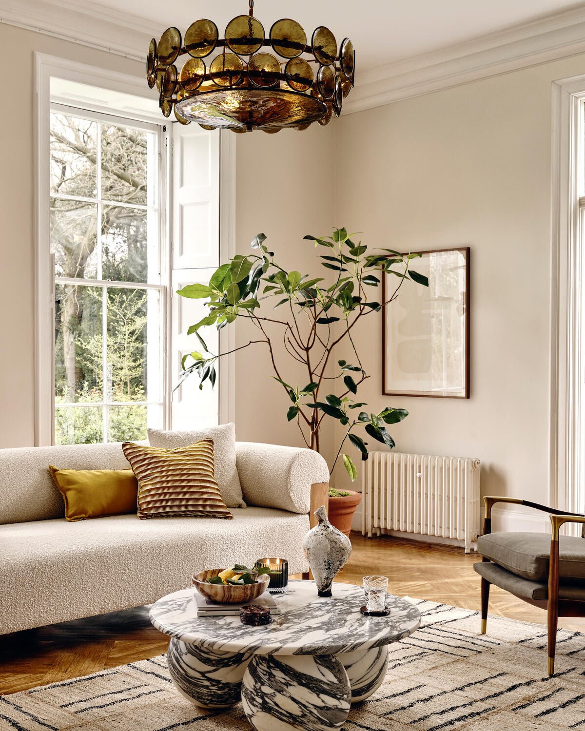Green-gold disc chandelier from Clérachic high above a marble coffee table, a cream sofa and a leafy plant in a bright room.