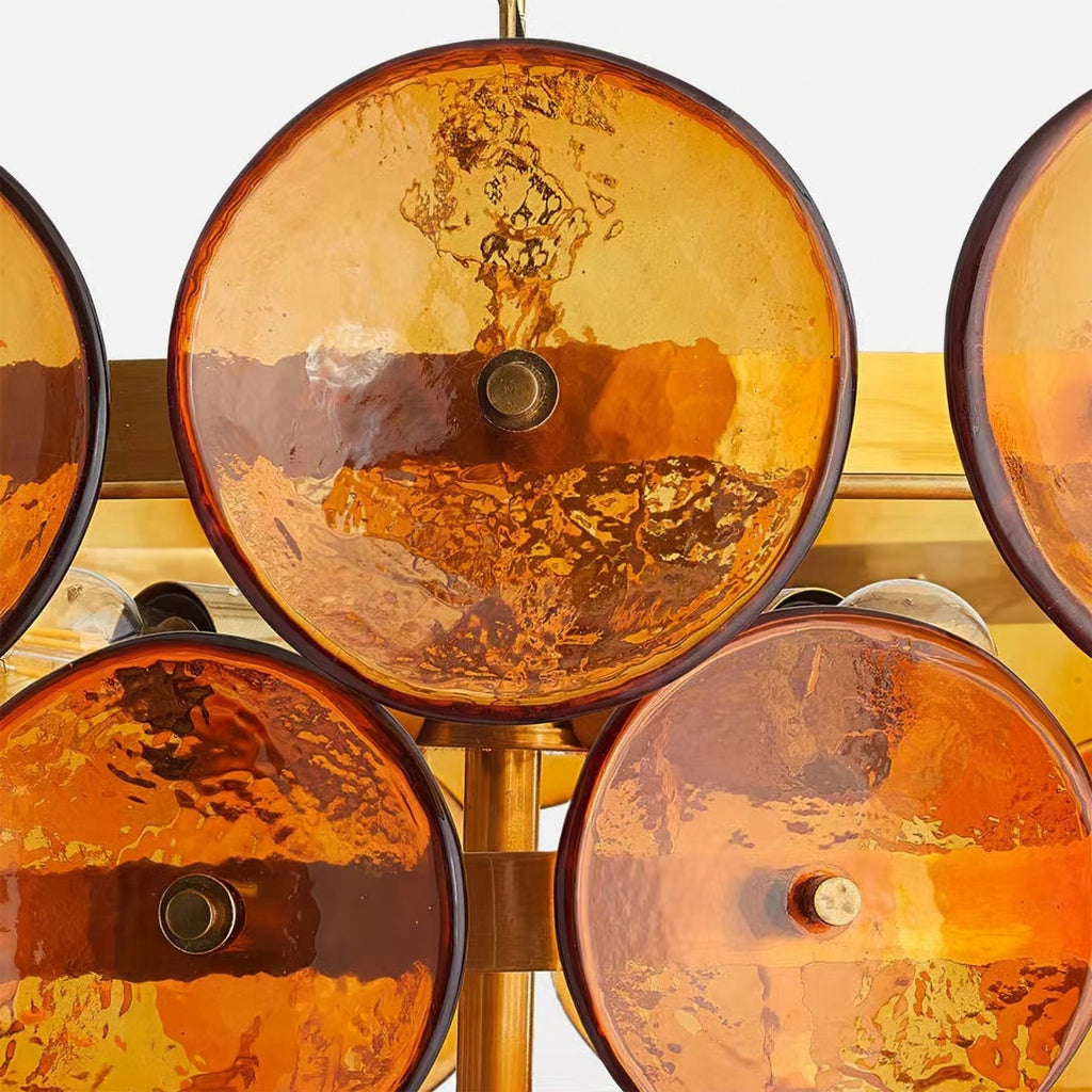Close view of large amber glass discs with dark rims, each fixed to the gold frame by a small brass stud, on this Clérachic chandelier.