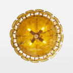 Looking up at the underside of this Clérachic chandelier, a glowing amber bowl ringed by overlapping gold-green glass discs.
