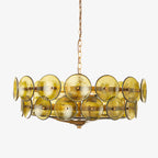 Close crop of the green-gold glass discs and the gold chain on a Clérachic chandelier, in front of a pale grey backdrop.