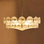 White frosted glass discs lit warm on this Clérachic chandelier, against a deep caramel-brown wall.