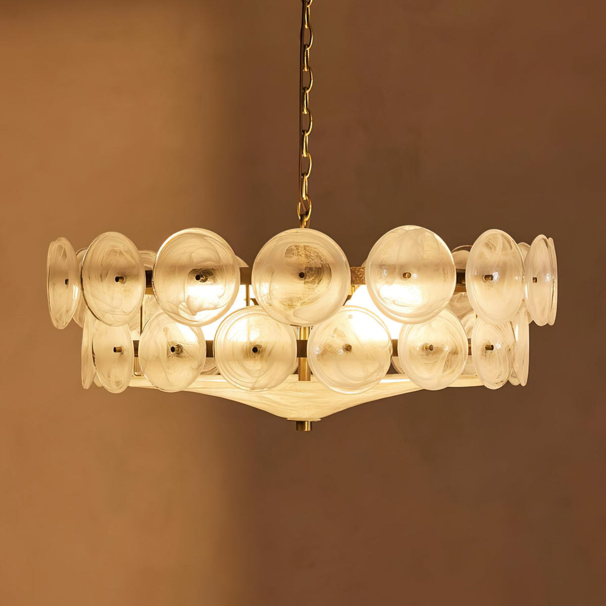 White frosted glass discs lit warm on this Clérachic chandelier, against a deep caramel-brown wall.