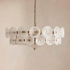 Frosted white swirled glass discs on a brass frame, this Clérachic chandelier hangs against a soft beige plaster wall.