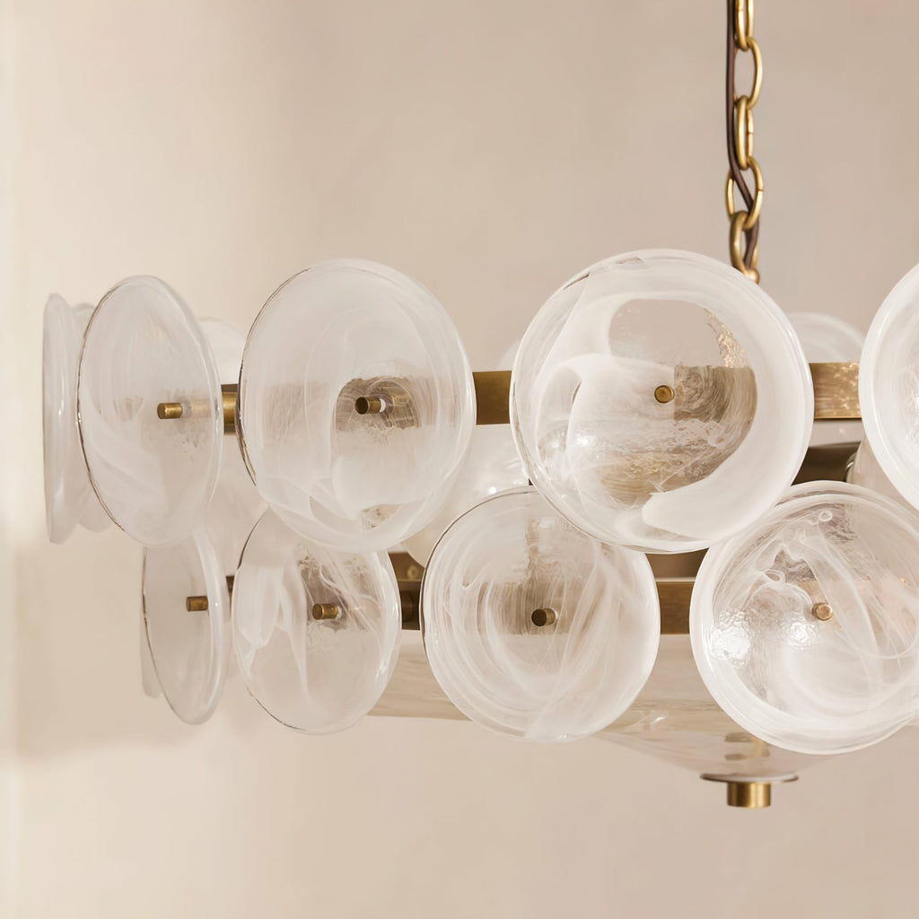 Close view of milky white swirled glass discs on a bronze-toned frame, from a Clérachic chandelier against a cream wall.