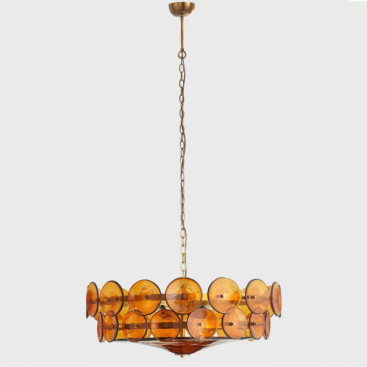 Small amber disc chandelier from Clérachic on a long thin chain, hanging in a grey studio space.