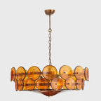 Amber glass disc chandelier from Clérachic with a brass canopy and a wide red-amber glass bowl underneath, on grey.