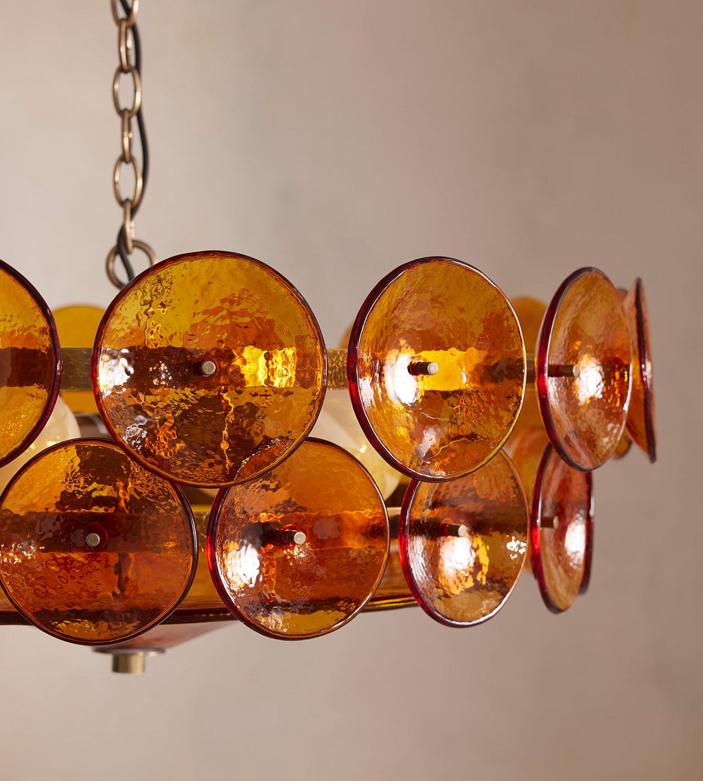 Close view of amber glass discs with ruby edges on a Clérachic chandelier, against a warm blush wall.