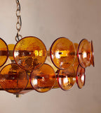 Close view of amber glass discs with ruby edges on a Clérachic chandelier, against a warm blush wall.