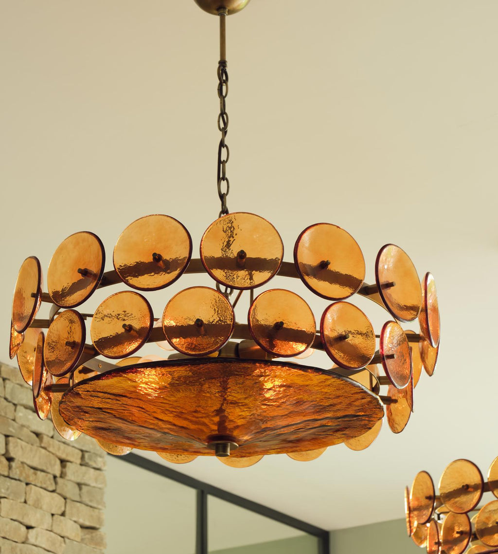Looking up at an amber disc chandelier from Clérachic in a room with a stone wall, the textured bowl glowing underneath.